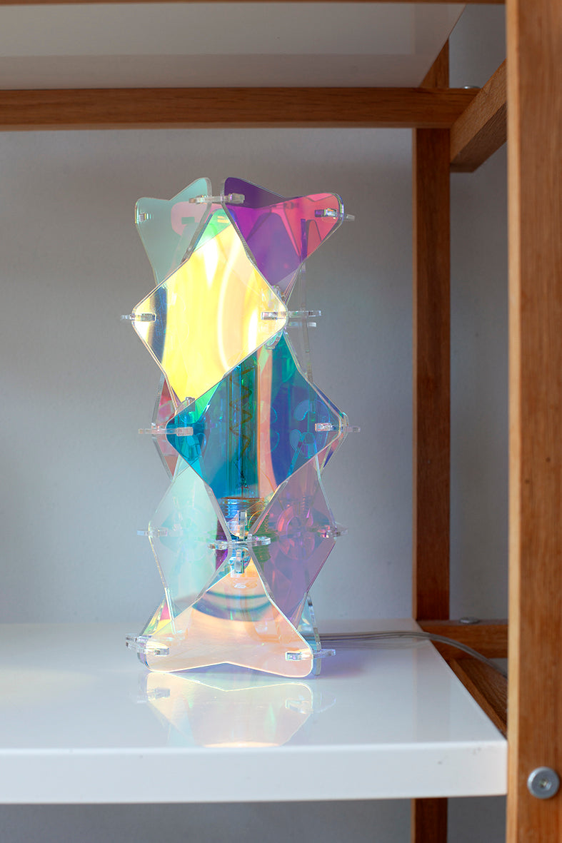 Een tafellamp in de kenmerkende irisiderende sfeer die je kent van Lux Vortex. De lamp is een tafelmodel en staat in een kast