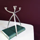 Space Age Aluminium Kandelaar voor drie kaarsen. Gefotografeerd op een witte tafel met een boek eronder als vergelijking voor grootte. Vintage van Atelier Aeris verkrijgbaar bij Draumr
