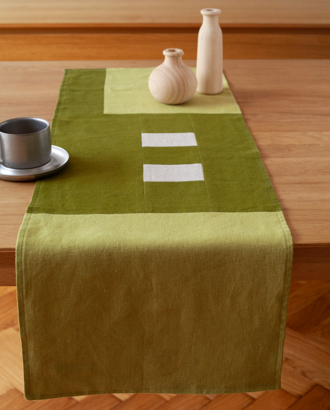 Een overzicht van een mos groene tafelrunner ontworpen door Kathryn Clark gedrapeerd over een houten tafel
