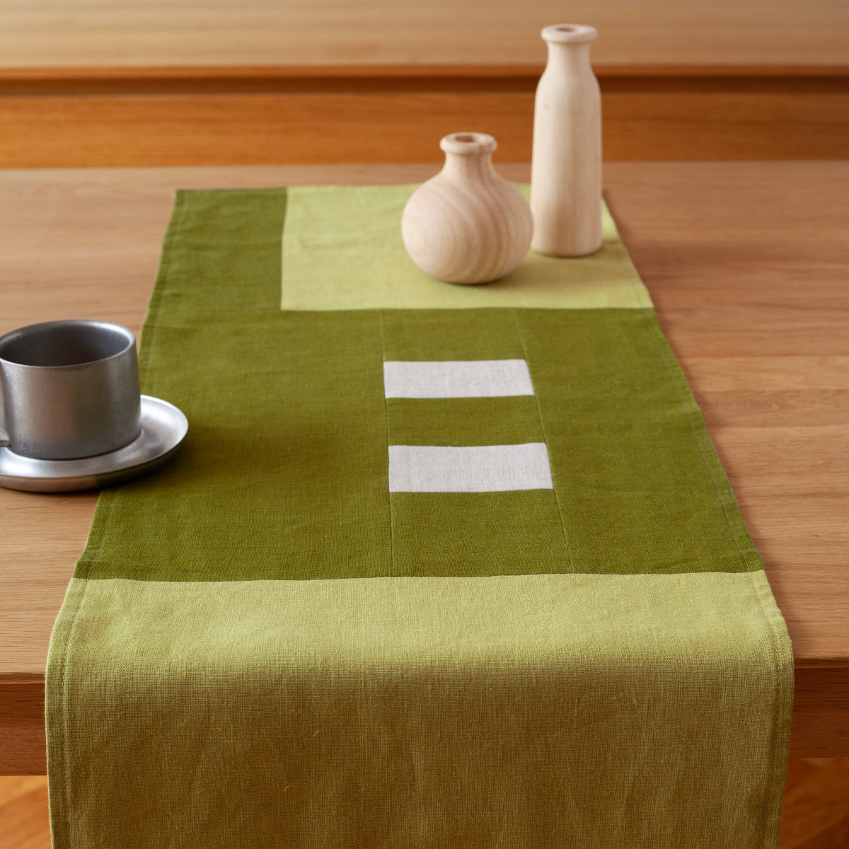 Een overzicht van een mos groene tafelrunner ontworpen door Kathryn Clark gedrapeerd over een houten tafel