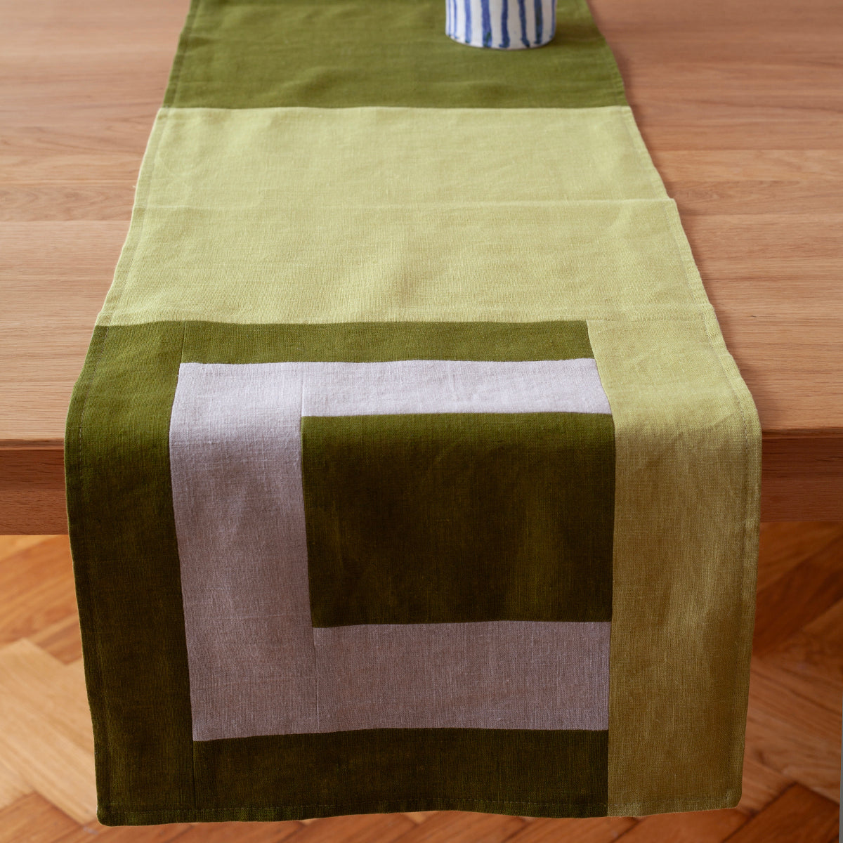 Een mos groene tafelrunner ontworpen door Kathryn Clark, liggend op een houten tafel in een interieursetting