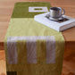 Een overzicht van een mos groene tafelrunner ontworpen door Kathryn Clark gelegd over een houten tafel met een boek en een koffiekopje