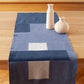 Een sfeervolle foto van een blauwe  tafelrunner ontworpen door Kathryn Clark, gedrapeerd over een houten tafel.