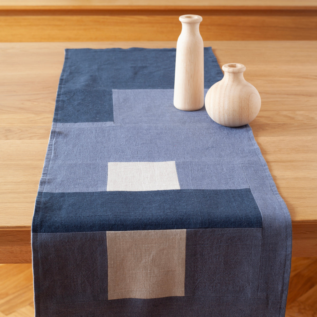 Een sfeervolle foto van een blauwe  tafelrunner ontworpen door Kathryn Clark, gedrapeerd over een houten tafel.