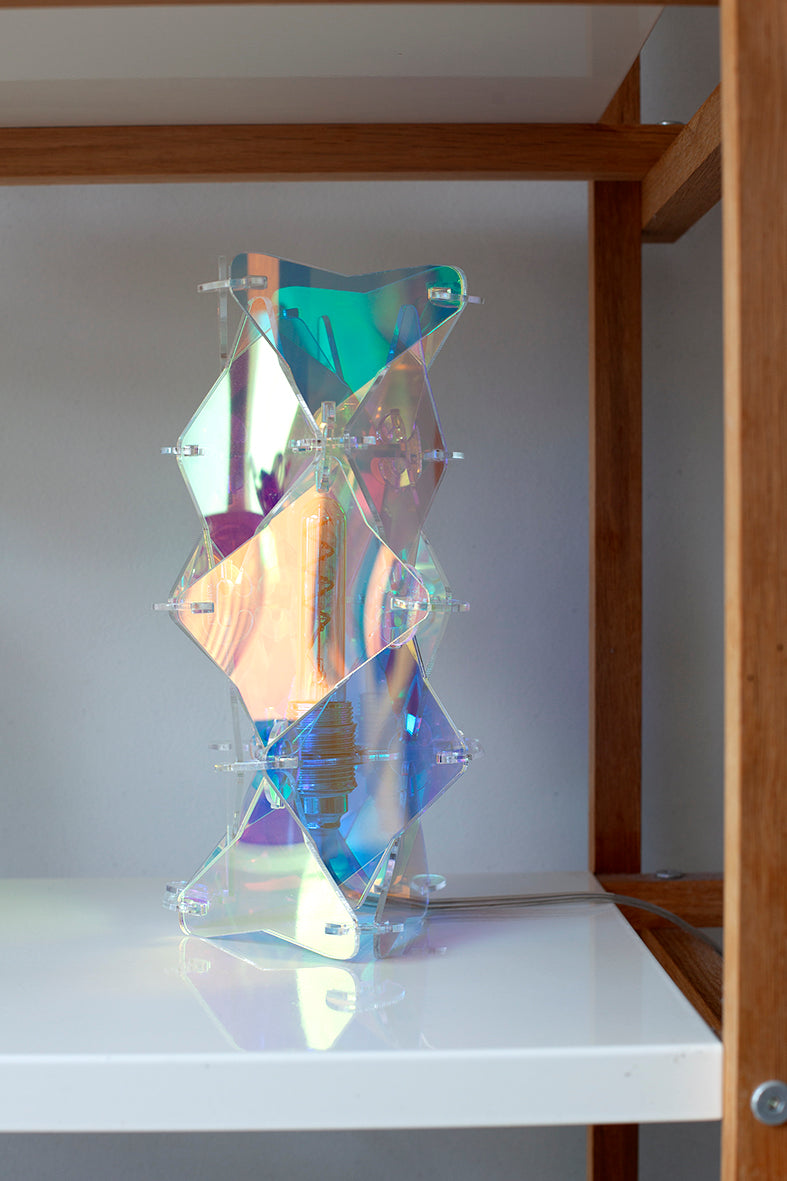 Een tafellamp in de kenmerkende irisiderende sfeer die je kent van Lux Vortex. De lamp is een tafelmodel en staat in een kast